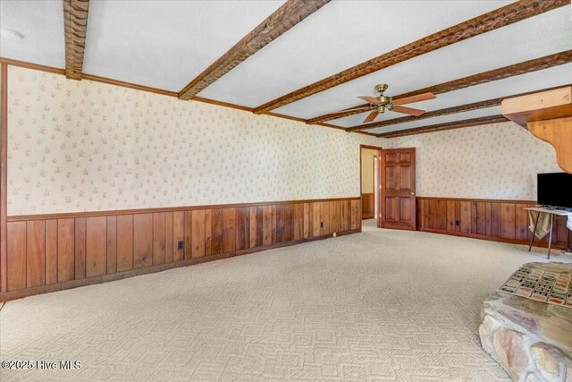 unfurnished room featuring wallpapered walls, beam ceiling, and a wainscoted wall