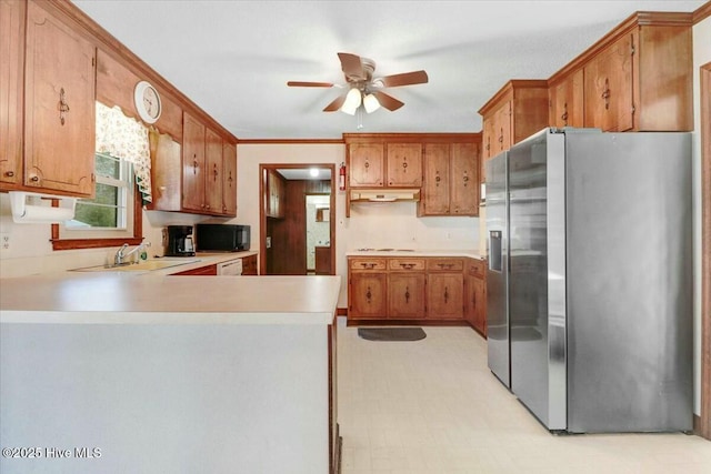 kitchen with stainless steel fridge, a peninsula, light countertops, black microwave, and a sink