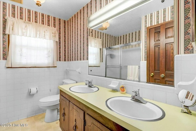 full bathroom with a stall shower, wainscoting, a sink, and wallpapered walls
