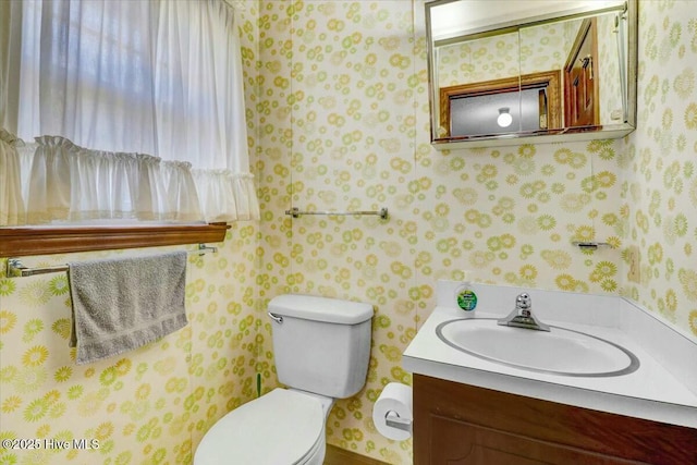 half bathroom featuring vanity, toilet, and wallpapered walls