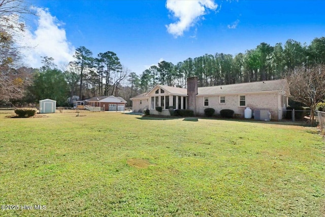 back of property featuring an outbuilding, a chimney, a lawn, a storage shed, and fence