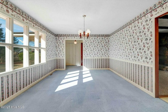 carpeted empty room featuring a notable chandelier, baseboards, and wallpapered walls