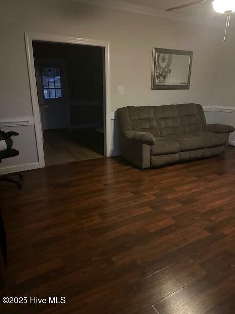 living room with crown molding, a ceiling fan, and dark wood-type flooring