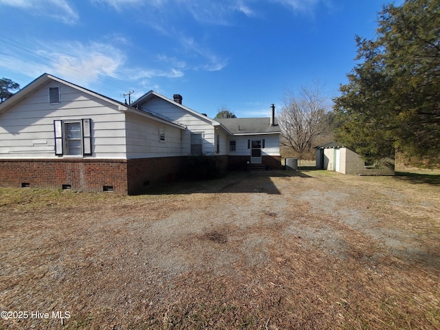 view of side of home featuring crawl space, a storage shed, an outdoor structure, and brick siding