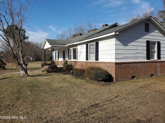 view of side of property featuring a porch, brick siding, crawl space, a lawn, and a chimney