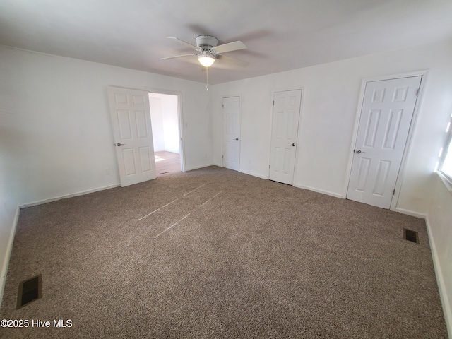 unfurnished bedroom featuring baseboards, visible vents, carpet flooring, and two closets