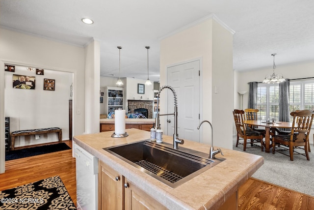 kitchen featuring a fireplace, light wood-style floors, a kitchen island with sink, a sink, and dishwasher