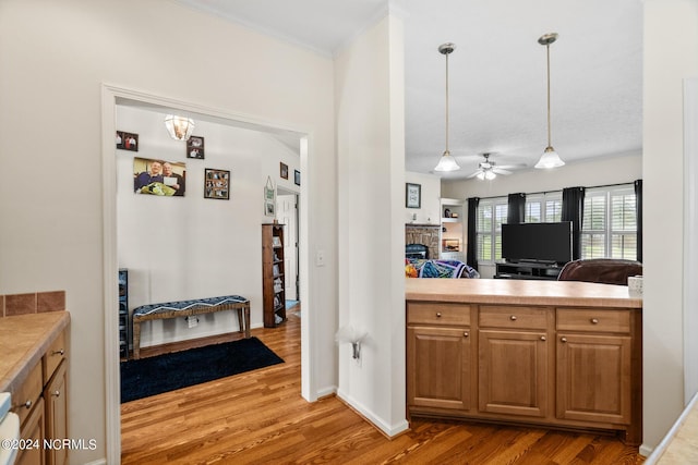 kitchen featuring a fireplace, wood finished floors, light countertops, hanging light fixtures, and brown cabinetry