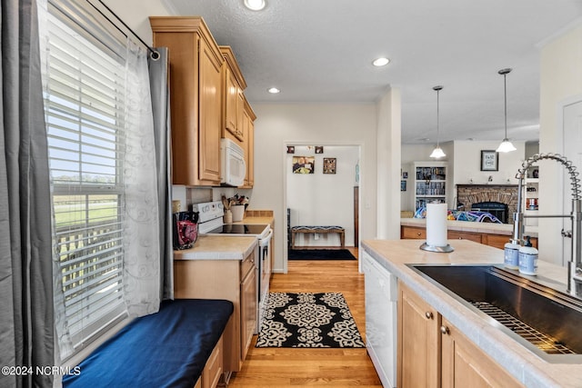 kitchen featuring white appliances, a fireplace, a sink, light wood-style floors, and light countertops