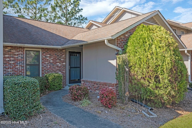 entrance to property with brick siding and a shingled roof