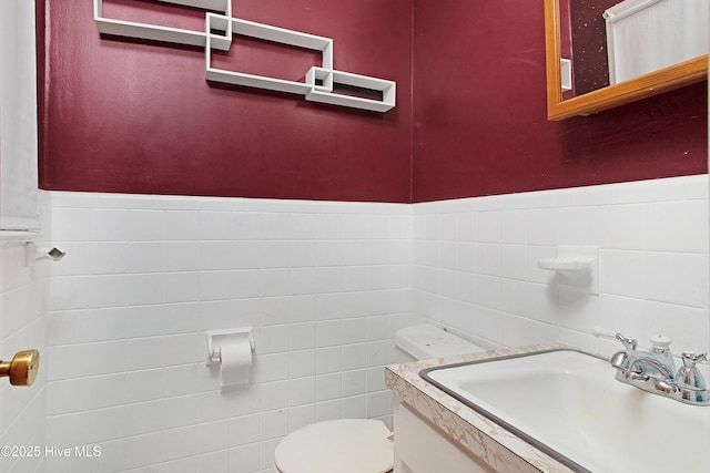 bathroom with tile walls, wainscoting, toilet, and vanity