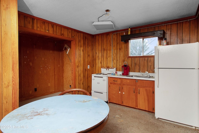 kitchen featuring white appliances, a sink, light countertops, wood walls, and light colored carpet