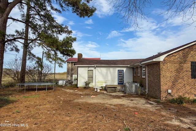 rear view of property with entry steps, crawl space, central air condition unit, a trampoline, and brick siding