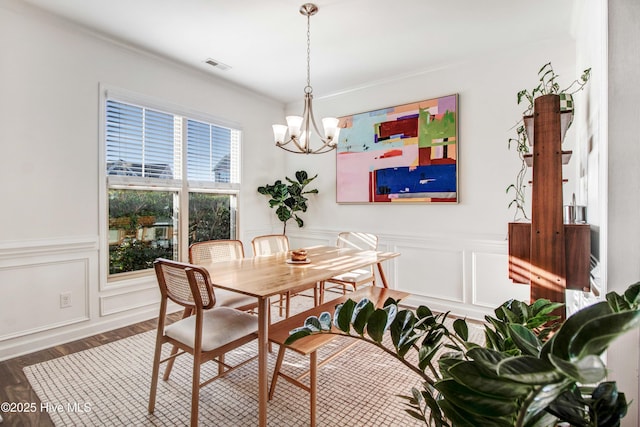 dining room featuring a decorative wall, a wainscoted wall, wood finished floors, visible vents, and an inviting chandelier