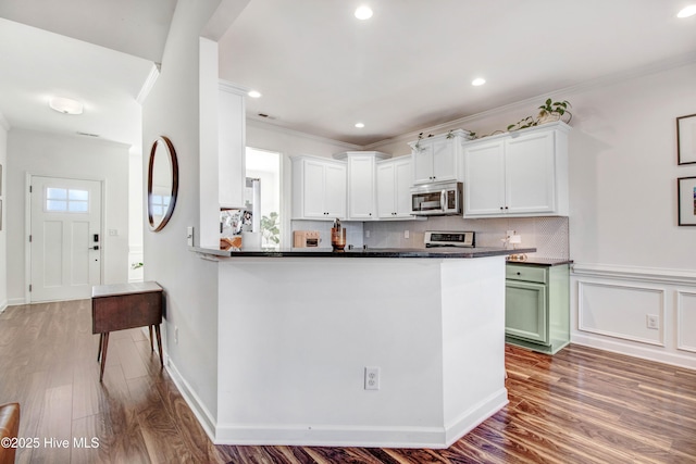 kitchen featuring tasteful backsplash, stainless steel microwave, ornamental molding, white cabinets, and wood finished floors