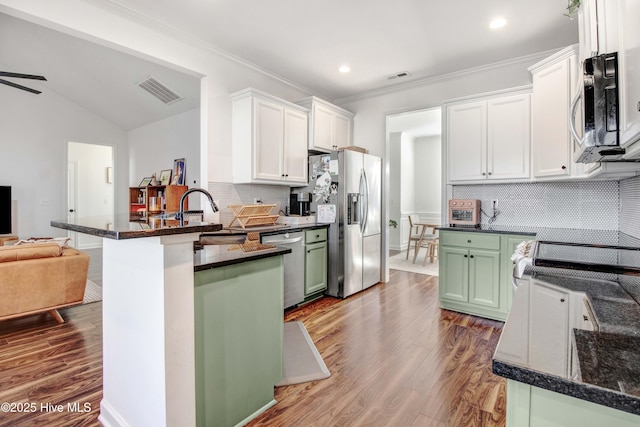 kitchen featuring stainless steel appliances, a peninsula, a sink, open floor plan, and green cabinets