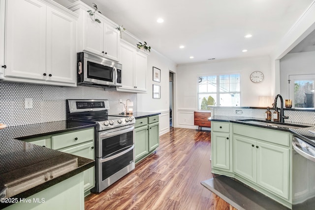 kitchen with stainless steel appliances, wood finished floors, a sink, ornamental molding, and green cabinetry