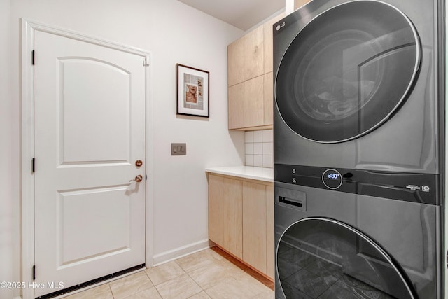 laundry room featuring light tile patterned floors, cabinet space, stacked washer and clothes dryer, and baseboards