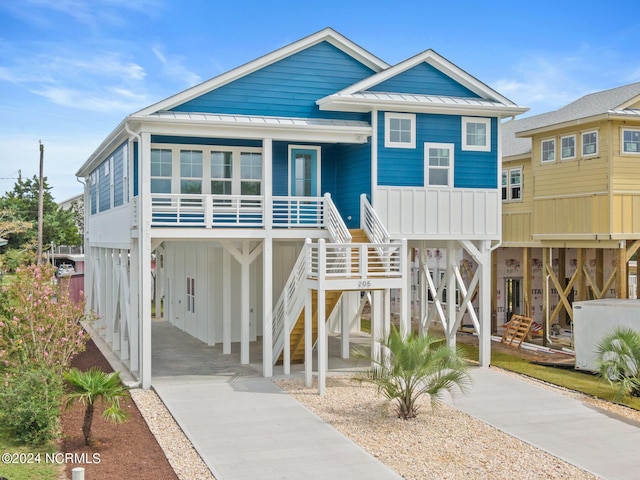 raised beach house featuring covered porch, a standing seam roof, metal roof, driveway, and stairs