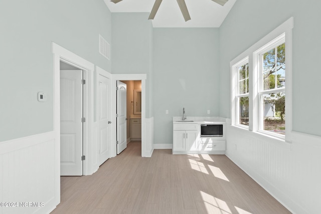 unfurnished bedroom featuring visible vents, wainscoting, a towering ceiling, light wood-style floors, and a sink