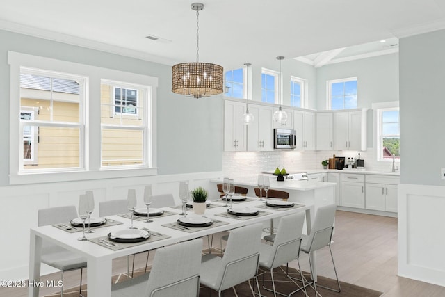 kitchen featuring white cabinets, a wainscoted wall, stainless steel microwave, ornamental molding, and a decorative wall