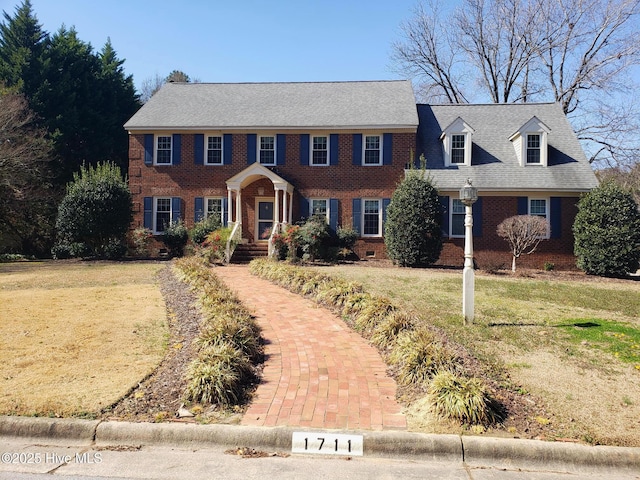 colonial-style house with crawl space, roof with shingles, a front lawn, and brick siding