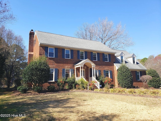 colonial-style house featuring a chimney, a front lawn, and brick siding