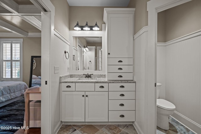 ensuite bathroom featuring wainscoting, vanity, toilet, and ensuite bathroom