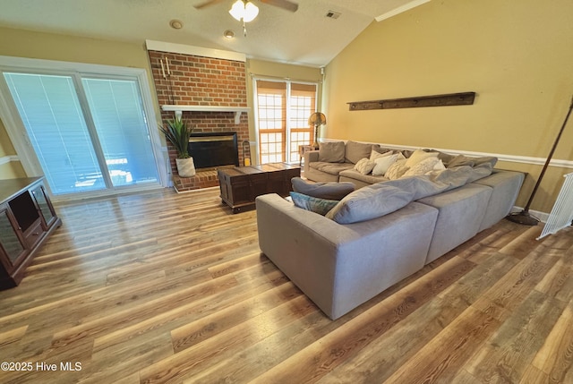 living area featuring ceiling fan, wood finished floors, visible vents, vaulted ceiling, and a brick fireplace