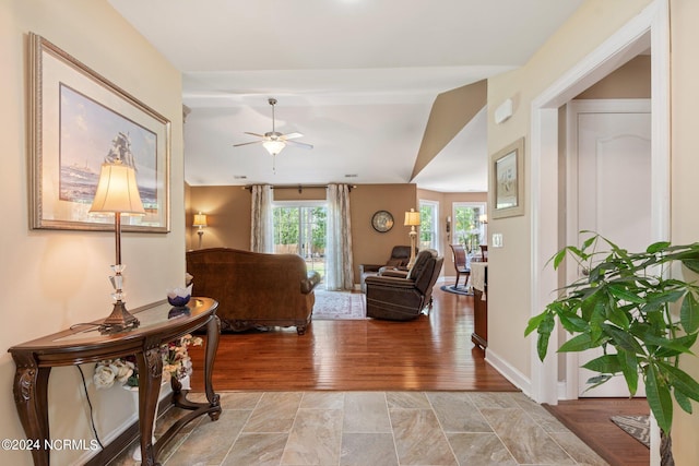 living room with a ceiling fan, vaulted ceiling, light wood-style flooring, and baseboards