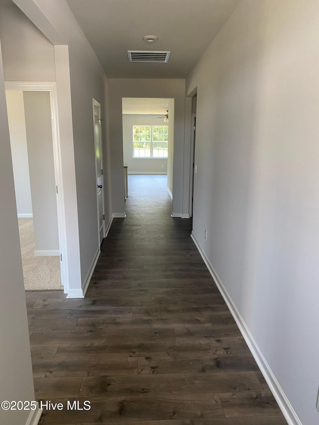 hall featuring dark wood-style flooring, visible vents, and baseboards