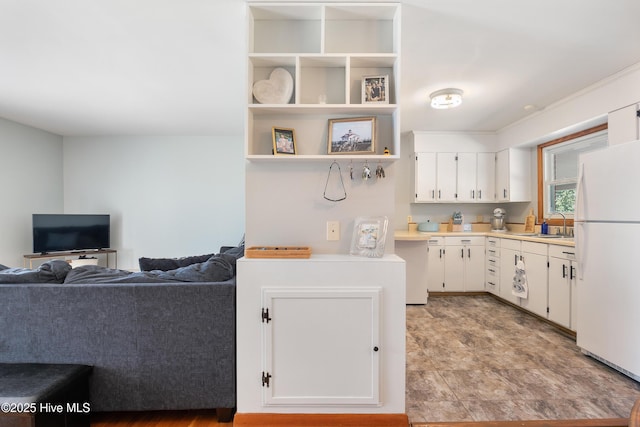 kitchen featuring open floor plan, freestanding refrigerator, light countertops, white cabinetry, and a sink