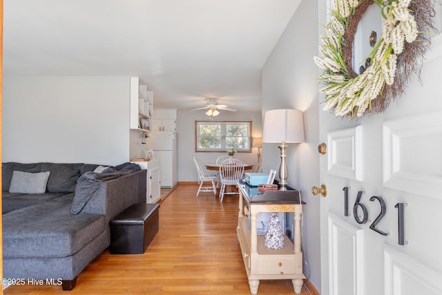 living room featuring baseboards, a ceiling fan, and light wood-style floors