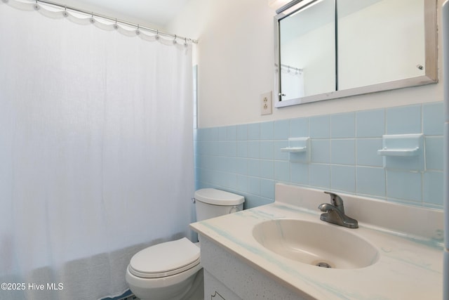 bathroom featuring wainscoting, vanity, toilet, and tile walls