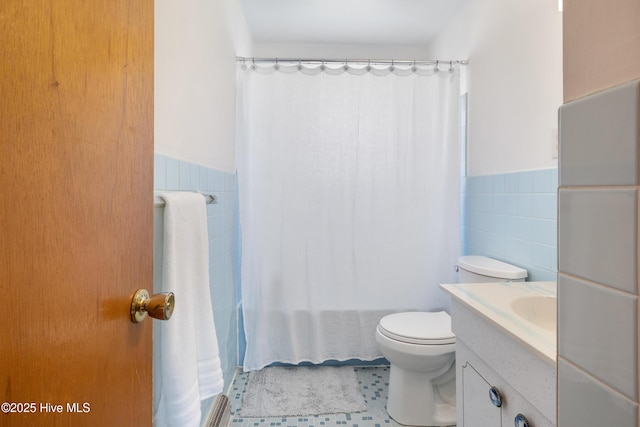 bathroom featuring tile walls, toilet, shower / bath combo with shower curtain, wainscoting, and vanity