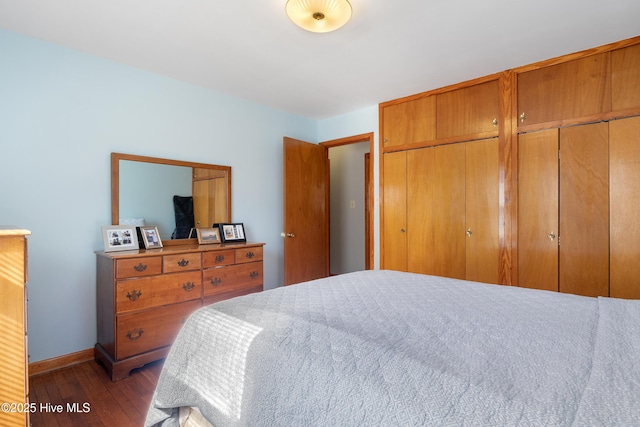 bedroom with hardwood / wood-style floors, two closets, and baseboards