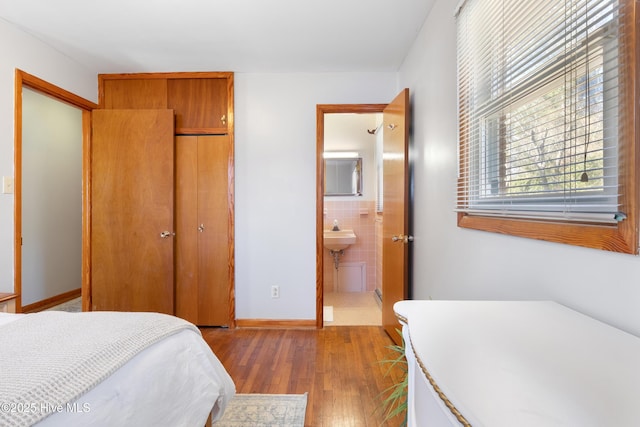 bedroom with wood finished floors, tile walls, baseboards, a closet, and ensuite bath