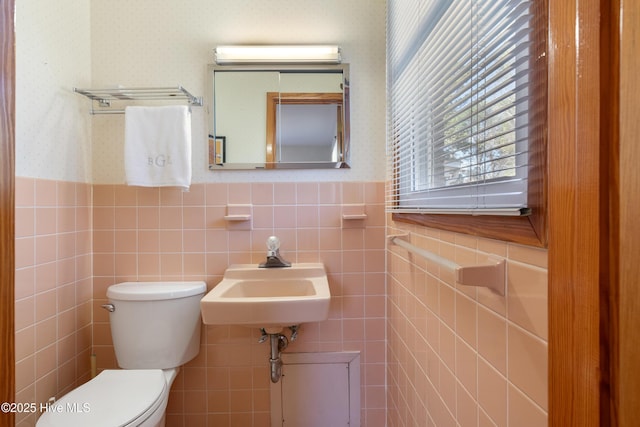 half bathroom with a wainscoted wall, a sink, toilet, and wallpapered walls