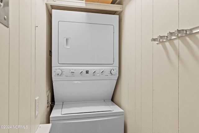 clothes washing area featuring laundry area, wooden walls, and stacked washer / dryer