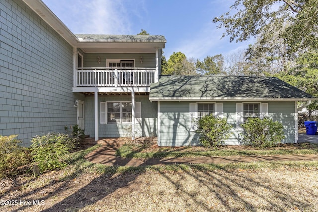 rear view of property featuring a balcony and a shingled roof