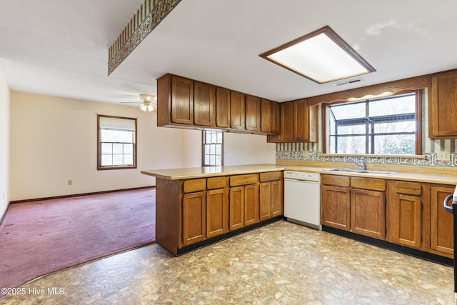 kitchen with brown cabinets, light countertops, a sink, dishwasher, and a peninsula