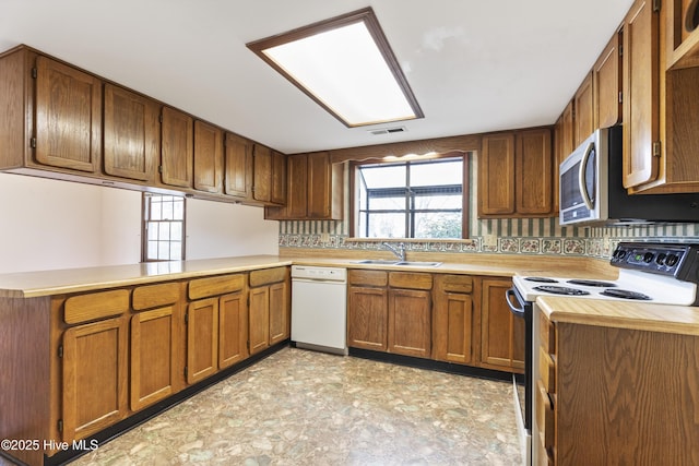 kitchen featuring electric range oven, brown cabinets, white dishwasher, light countertops, and a sink