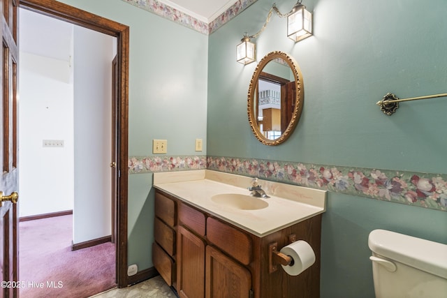 bathroom featuring baseboards, vanity, toilet, and wallpapered walls