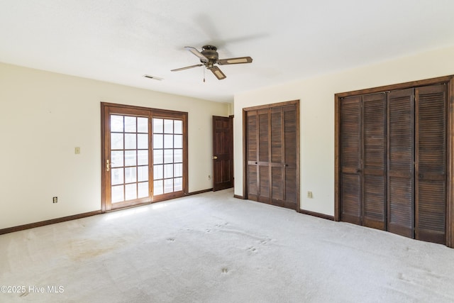 unfurnished bedroom with light carpet, baseboards, visible vents, a ceiling fan, and two closets