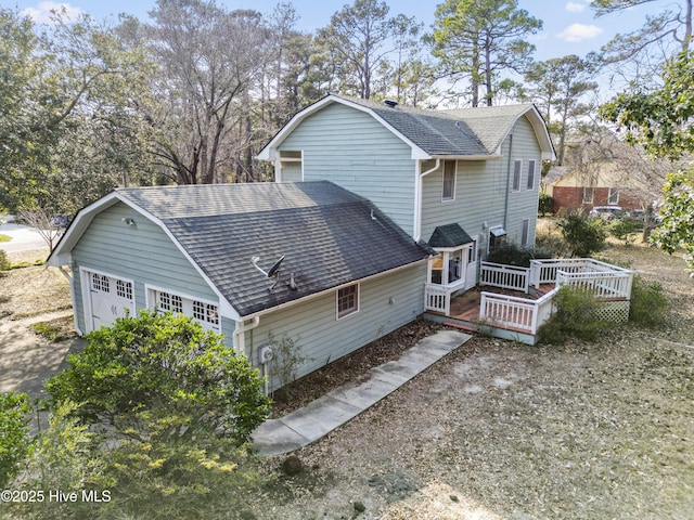 rear view of property with a garage, a deck, a gambrel roof, and roof with shingles