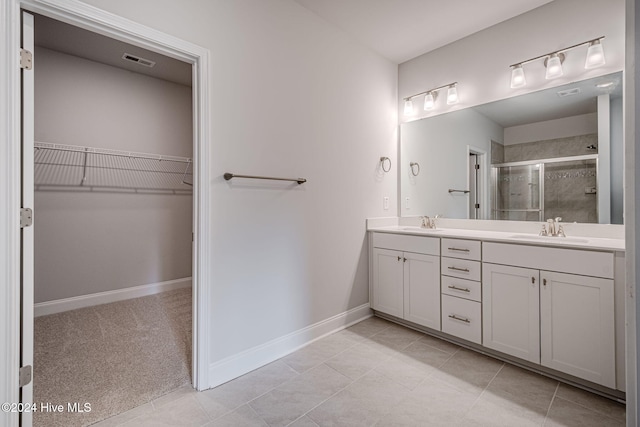 bathroom featuring double vanity, a stall shower, baseboards, a spacious closet, and a sink