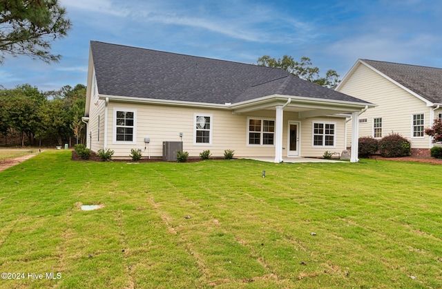 rear view of property featuring central air condition unit, a patio area, a shingled roof, and a yard