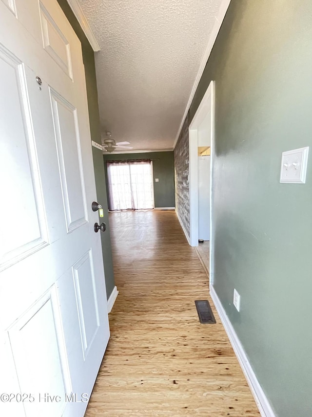 hall featuring visible vents, ornamental molding, a textured ceiling, and wood finished floors