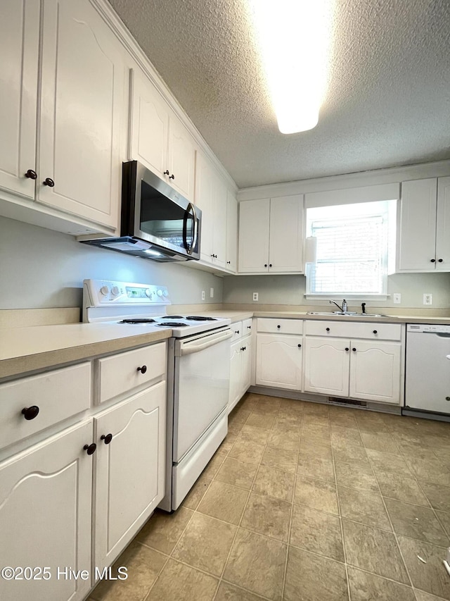 kitchen with white appliances, a sink, visible vents, white cabinets, and light countertops