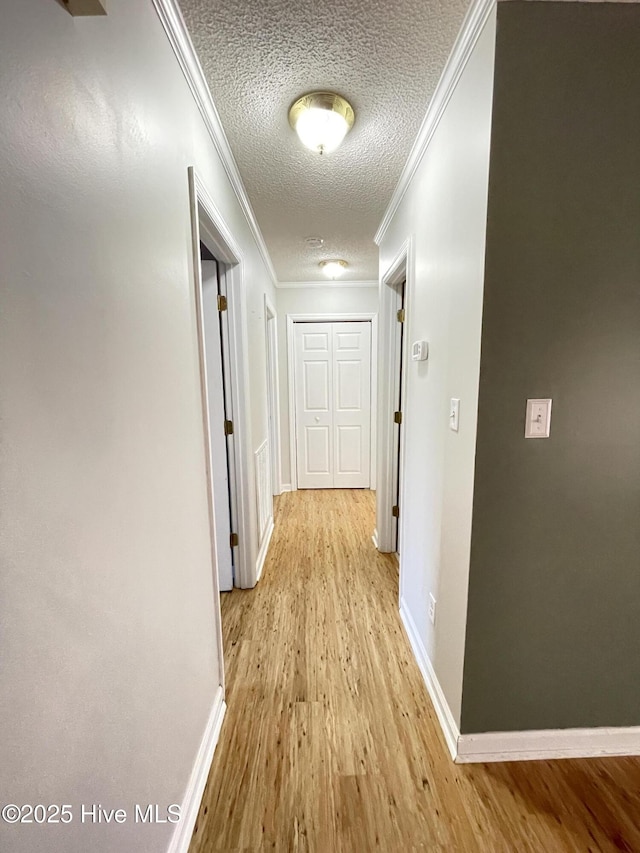 corridor featuring baseboards, light wood-style flooring, ornamental molding, and a textured ceiling